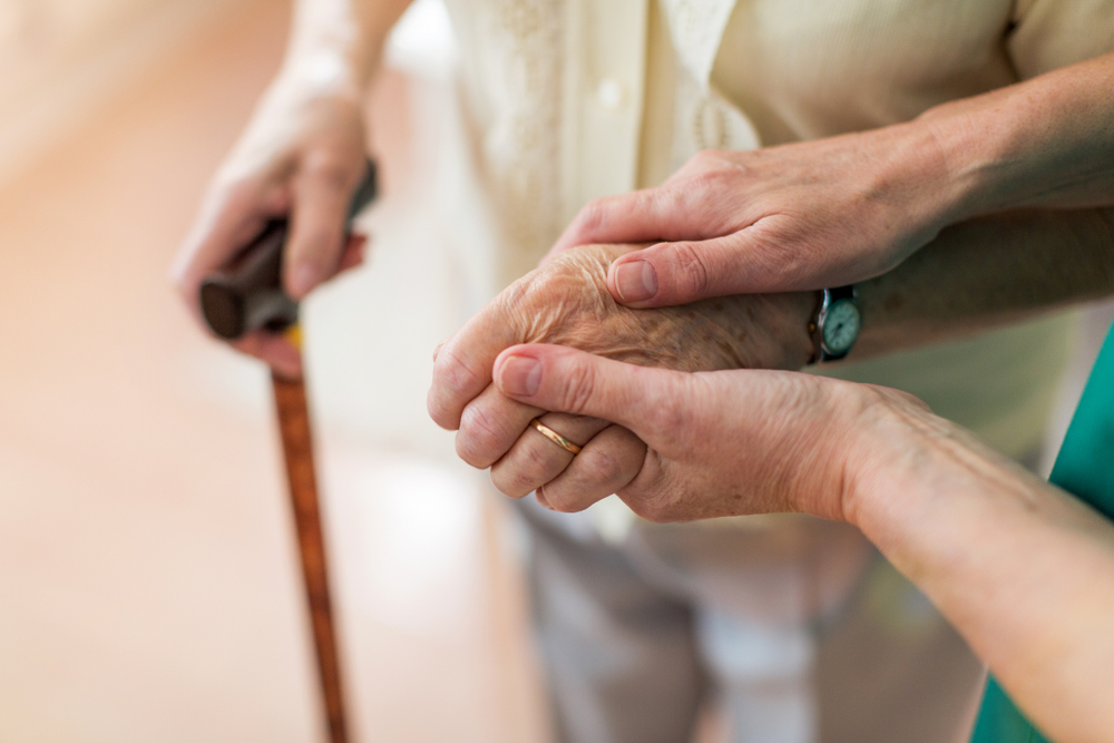 Carer holding the hand of an elderly dementia patient during dementia care at home.